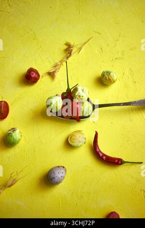 Légumes frais et œufs de caille sur un fond jaune vif. Choux de Bruxelles, piments et tomates disposés de manière créative pour une alimentation saine et Banque D'Images