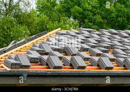 Piles de tuiles grises placées sur des chevrons en bois pendant le processus d'installation de toiture de maison neuve Banque D'Images