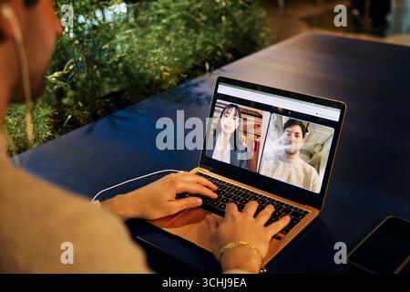 Jeune homme professionnel des affaires discutant en appel vidéo avec une collègue féminine via un ordinateur portable sur un lieu de travail hybride Banque D'Images