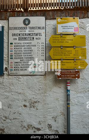 Panneau jaune vif indiquant les directions pour les routes et les sentiers, monté sur un mur blanc à Dürnstein, Autriche. Scène de village historique ensoleillée avec cobb Banque D'Images