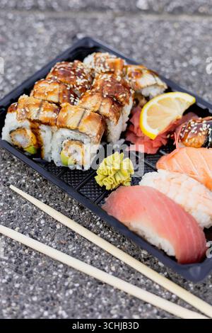 Un assortiment coloré de sushis et de sashimis présentés sur un plateau noir, avec des rouleaux d'anguille et des tranches fraîches de thon, de saumon et de crevettes, accompagnés de Banque D'Images