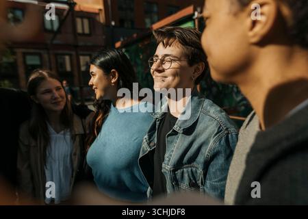 Jeune homme souriant debout avec les yeux fermés avec des amis au jour ensoleillé Banque D'Images