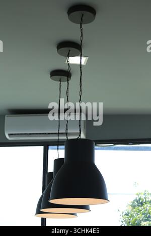 Trois suspensions noires modernes suspendues à un plafond élégant, offrant un éclairage contemporain dans un espace minimaliste avec une unité de climatisation Banque D'Images
