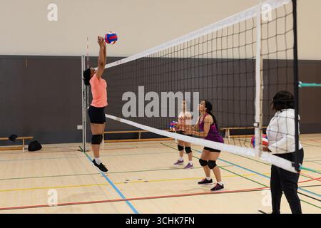 Diverses coéquipières féminines pratiquant le volley-ball au filet sur le terrain dans la salle de gym, volley-ball, espace copie Banque D'Images