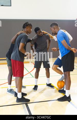Divers partenaires masculins se blottissant sur un terrain de basket-ball de gymnastique avec basket-ball orange et banc Banque D'Images