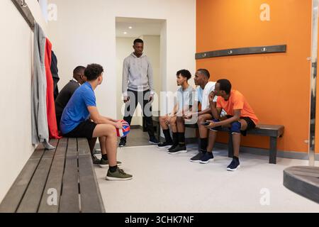 Équipe masculine diversifiée de volleyball se réunissant pour parler à l'entraîneur sur des bancs dans le vestiaire avec volleyball Banque D'Images