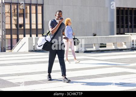 Divers amis en vêtements de sport marchant à travers la plaza au bureau parlant dans smartphone Banque D'Images