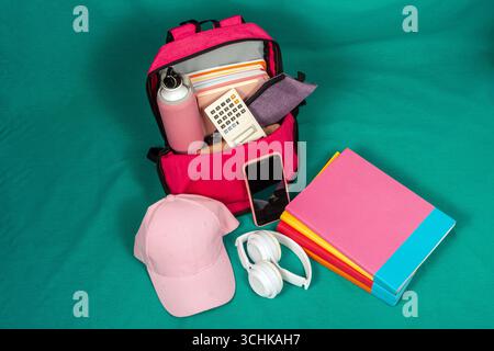 Sac à dos plein de fournitures scolaires prêtes pour étudier sur fond vert Banque D'Images