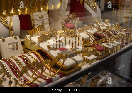 gros plan d'une vitrine de magasin remplie de divers types de bijoux en or, y compris des colliers, des bracelets et des bagues. Les éléments sont affichés en blanc et Banque D'Images