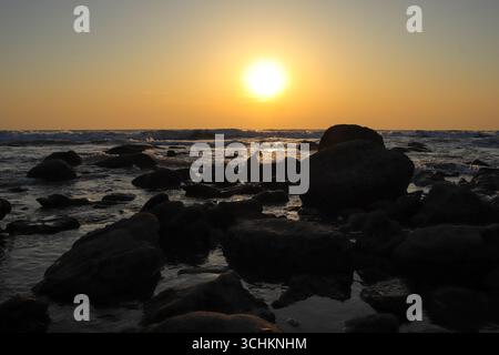 Le soleil se couche sur la baie du Bengale à Inani Beach, projetant une lueur dorée chaude à travers les vagues et les rochers silhouettes le long du rivage. Le monde est Banque D'Images