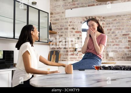Riant ensemble dans la cuisine moderne, deux jeunes femmes profitent du moment léger Banque D'Images