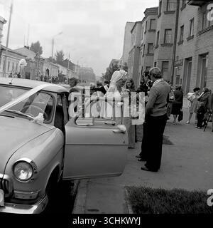Photos d'archives en noir et blanc prises dans la ville de Sloviansk en 1976. Les cadres capturent la procession du mariage près des anciens ZAGS (bureau d'enregistrement) sur la rue Lénine. Les jeunes mariés montent dans des voitures soviétiques décorées, une prestigieuse gaz-21 'Volga' et une VAZ 'Zhiguli' à la mode. Les scènes de rue transmettent l'atmosphère animée et les traditions d'un mariage soviétique, ainsi que le look quotidien de Sloviansk dans les années 1970 Banque D'Images