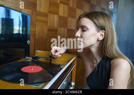 une photo romantique vintage, jeune femme met sur un disque vinyle assis sur le sol, musique rétro, soirée romantique isolée Banque D'Images