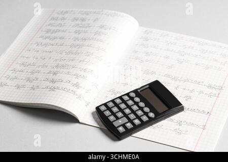 Copybook avec formules mathématiques manuscrites et calculatrice sur fond gris Banque D'Images