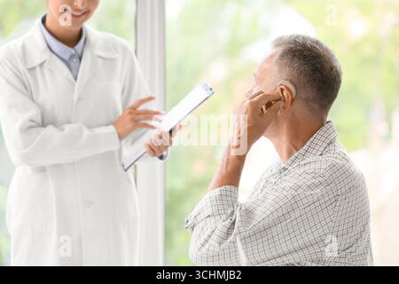 Homme mature avec prothèse auditive visitant le médecin en clinique Banque D'Images