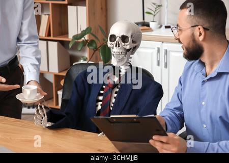 Collègues masculins avec squelette humain travaillant à table dans le bureau Banque D'Images