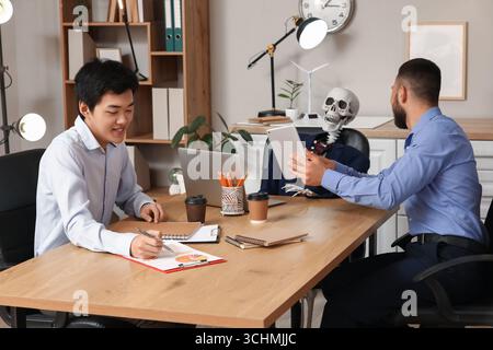 Collègues masculins avec squelette humain travaillant à table dans le bureau Banque D'Images