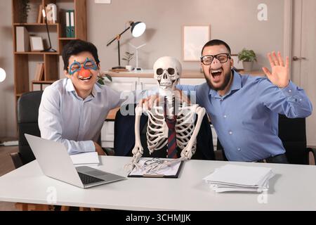 Collègues masculins avec déguisement drôle et squelette humain à table dans le bureau Banque D'Images