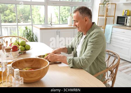 Homme mature coupant la pomme pour le cidre à table dans la cuisine Banque D'Images