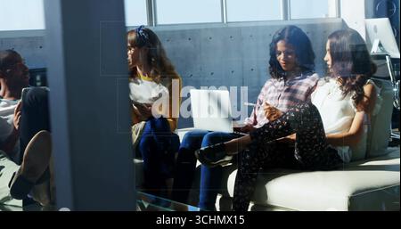 Groupe de quatre collègues discutant des idées dans le salon du bureau, avec tablette et ordinateur portable Banque D'Images