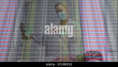 Discutant des données de stock, les professionnels pointant à l'affichage numérique à côté de la cloison en verre dans le bureau Banque D'Images