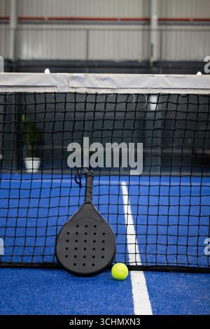 Raquette de padel appuyée contre le filet sur un court bleu avec des lignes blanches, balle de tennis jaune au repos Banque D'Images