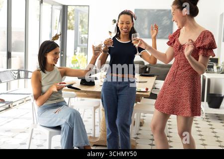 Riant et riant des lunettes, trois jeunes femmes célèbrent dans la salle à manger ensoleillée Banque D'Images