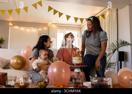Diverses amies féminines célébrant l'anniversaire avec un gâteau et des ballons, souriant et appréciant, à la maison Banque D'Images