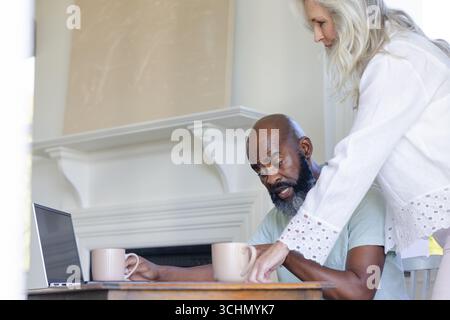 Couple mûr appréciant le café ensemble à la maison, en utilisant un ordinateur portable sur la table Banque D'Images