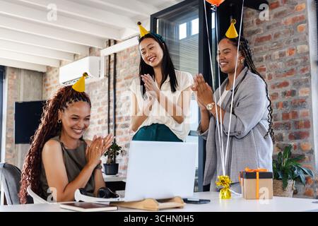 Diverses collègues féminines célébrant avec des chapeaux de fête et des cadeaux dans un cadre de bureau moderne Banque D'Images