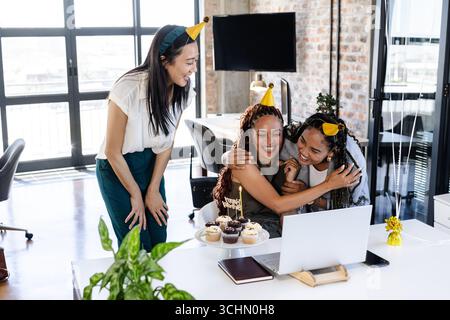 Diverses collègues féminines célébrant l'anniversaire avec des cupcakes et des rires dans un bureau moderne Banque D'Images