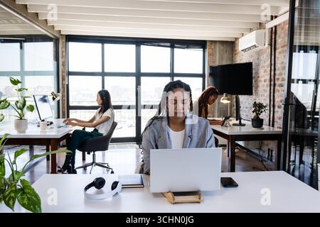 Focalisé divers professionnels féminins travaillant sur des ordinateurs portables dans un bureau moderne avec de grandes fenêtres Banque D'Images