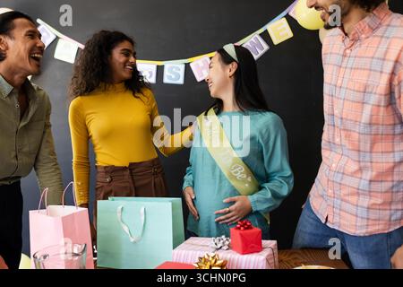 Célébrer la douche de bébé, des amis donnant des cadeaux et rire avec la future mère, au bureau Banque D'Images