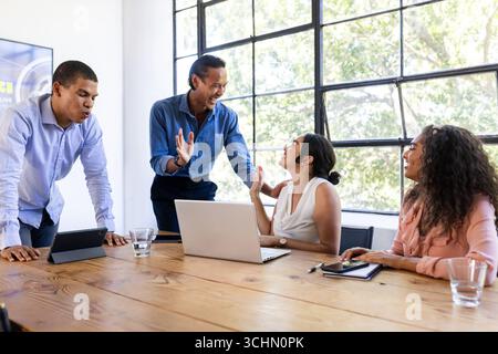 Équipe d'affaires diversifiée collaborant autour de la table, discutant des idées avec enthousiasme, au bureau Banque D'Images