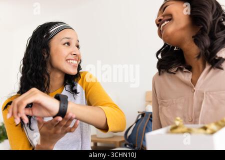 Jeune femme souriante montrant smartwatch à un ami tout en étant assis ensemble à la maison Banque D'Images