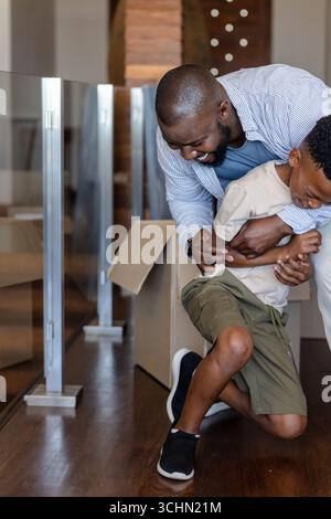 Père et fils jouant joyeusement à la maison près de boîtes en carton, collant ensemble Banque D'Images
