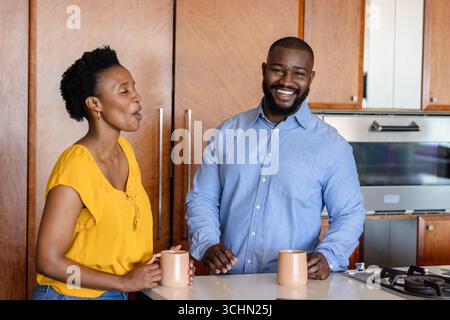 Couple appréciant le café et la conversation dans la cuisine moderne, souriant ensemble Banque D'Images
