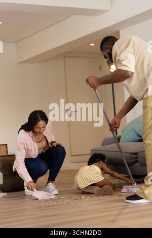Nettoyage du salon, famille afro-américaine balayant pendant que l'enfant aide les parents Banque D'Images