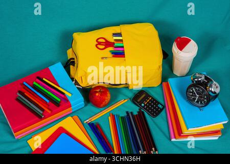 Sac à dos jaune, papeterie colorée et fournitures scolaires sur fond turquoise Banque D'Images
