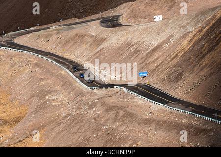 Une vue en grand angle d'une autoroute de montagne sinueuse et inversée traversant un terrain escarpé et rocheux avec un petit convoi de voitures. Banque D'Images