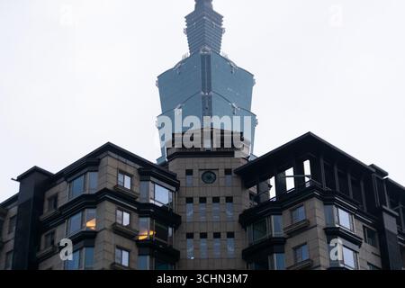 L'emblématique tour Taipei 101 encadrée par un bâtiment moderne en pierre par un jour brumeux et couvert. Banque D'Images