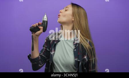 Femme tenant une perceuse électrique en toute confiance devant un fond violet vibrant, mettant en valeur l'indépendance, l'autonomisation et l'esprit de bricolage moderne. Banque D'Images