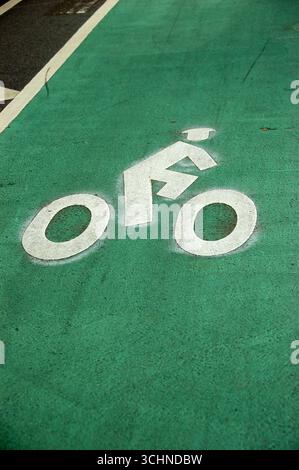 Symbole blanc de piste cyclable peint sur une surface asphaltée verte, indiquant une piste cyclable dédiée aux cyclistes en milieu urbain Banque D'Images