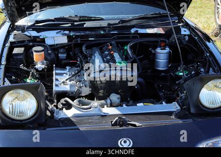 Cette image montre une Mazda MX-5, peut-être un modèle de première génération, avec son capot ouvert, révélant un compartiment moteur propre et bien entretenu. La voiture a des phares escamotables et un extérieur noir. Le moteur semble être l'original, présentant un radiateur et divers réservoirs de liquide. Illustration, éditorial : le rallye automobile de Stokes Bay à Gosport, Hampshire, Angleterre. 25 août 2025. Banque D'Images