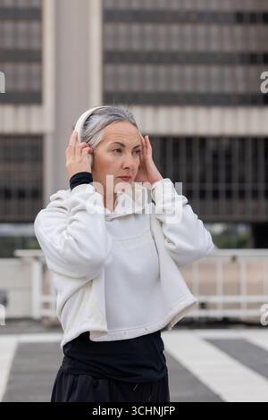 Femme ajustant les écouteurs sans fil tout en portant un sweat à capuche, pantalon de sport sur la terrasse sur le toit Banque D'Images