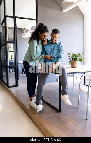 Divers collègues dans un bureau moderne souriant tout en regardant leur smartphone ensemble Banque D'Images