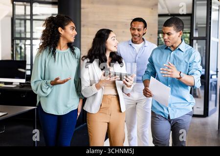 Équipe d'affaires diversifiée discutant du projet tout en marchant à travers le couloir de bureau moderne Banque D'Images
