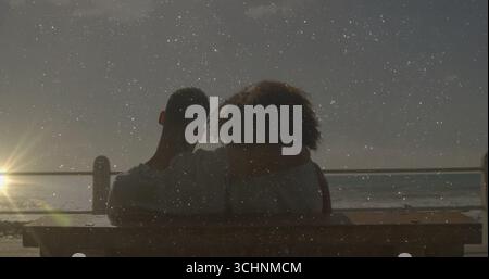 Regarder un couple adulte embrassant sur un banc en bois par la mer, avec garde-corps en métal et horizon de soleil brillant Banque D'Images
