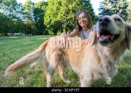 Femme souriant tout en caressant Golden retriever dans le parc illustrant la connexion joyeuse avec la nature et les animaux de compagnie Banque D'Images