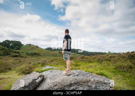 Homme debout sur un grand rocher dans les landes avec ciel dramatique au-dessus, bien-être dans la nature un jour d'été, homme en short et t-shirt dans la nature Banque D'Images